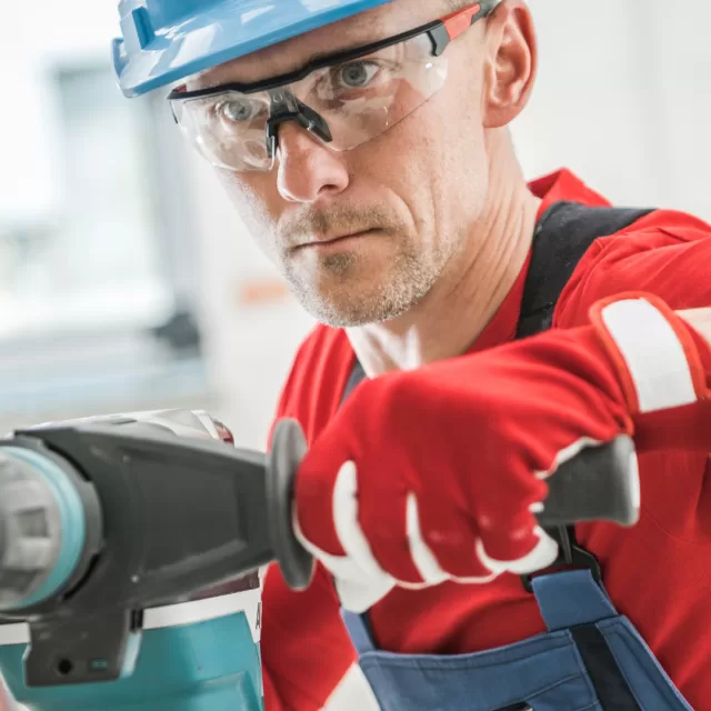 Trabalhador com capacete e óculos de proteção a utilizar uma ferramenta elétrica