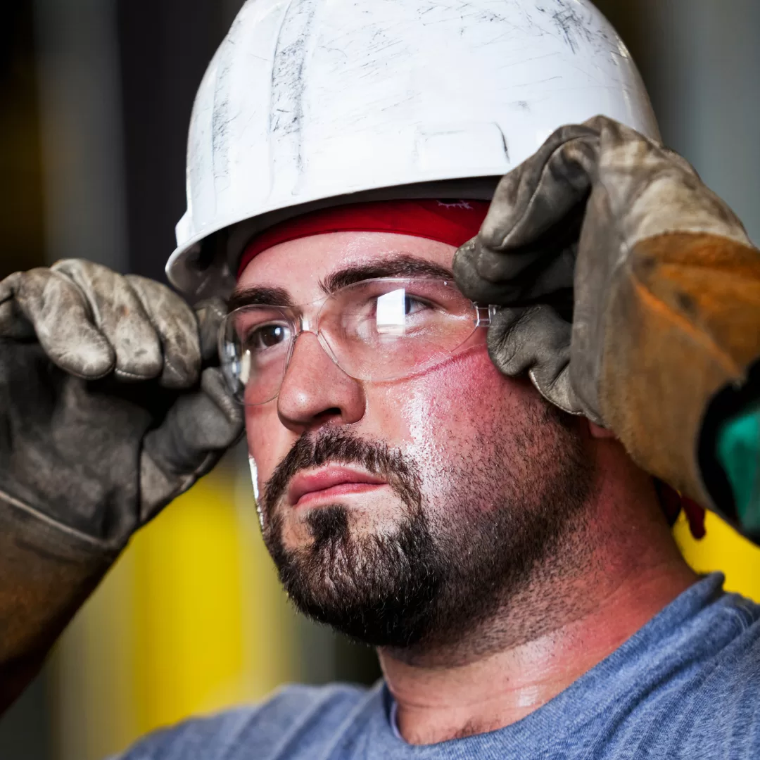 Trabalhador com capacete e óculos de proteção a ajustar os óculos no local de trabalho